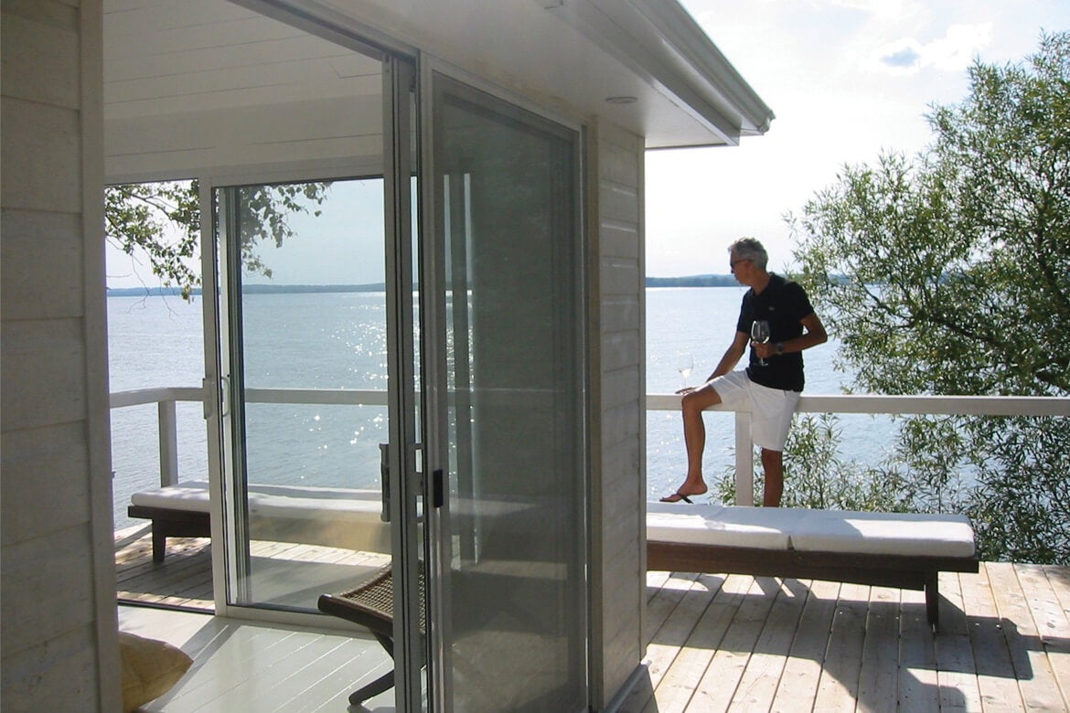 House on the edge of the water with owner drinking wine by the railing