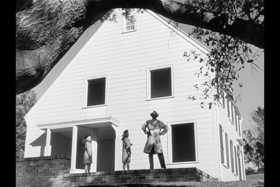 People looking at large white house from long ago